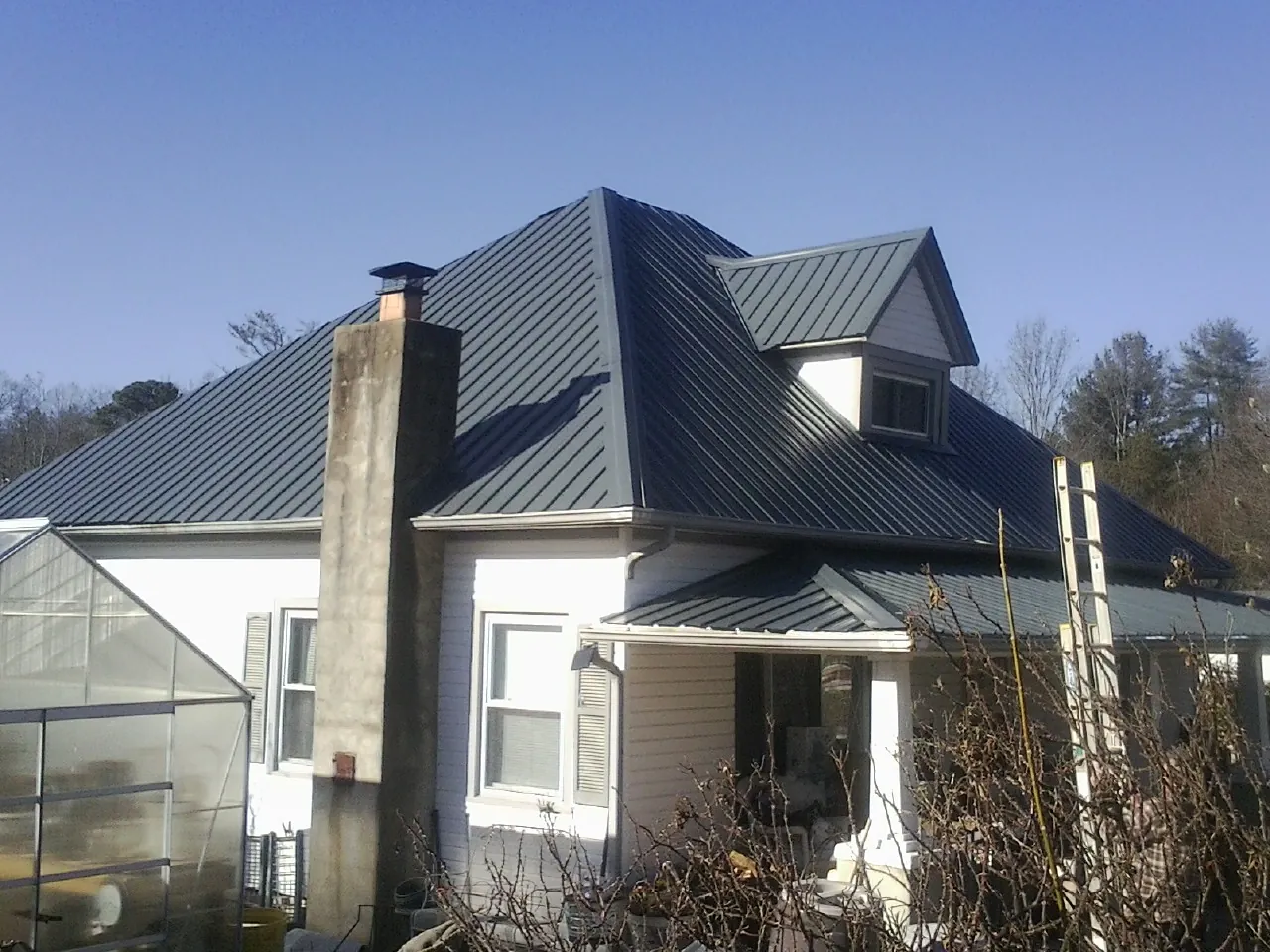 Dark blue standing seam metal roof on a white farmhouse with dormer — Slate & Tile Roof Repair by Roofing Brothers in Badin
