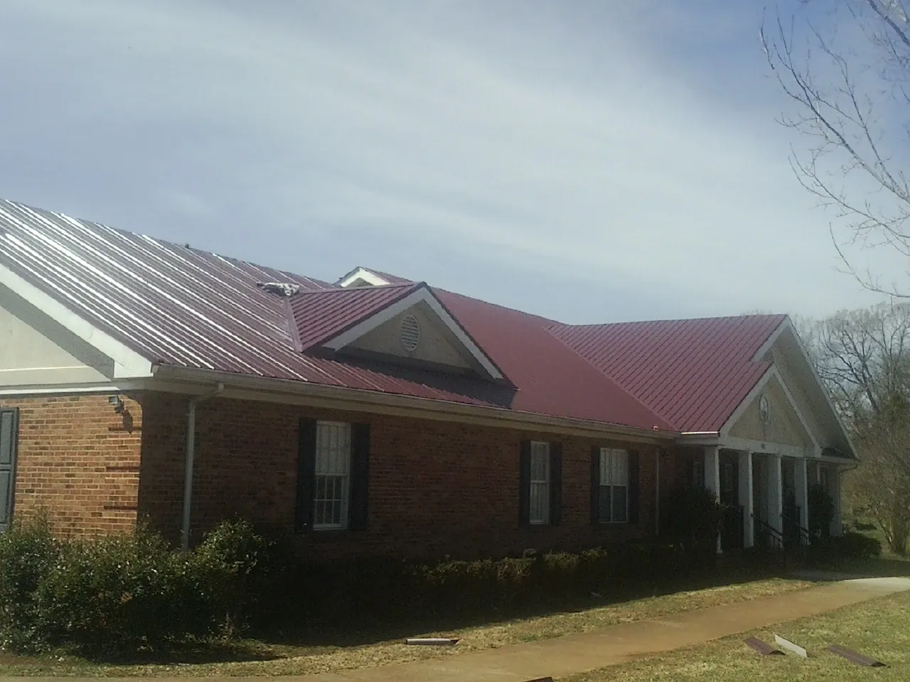 Red metal roof with gabled entries on a long brick building, from a Hail Damage Roof Repair job in Badin