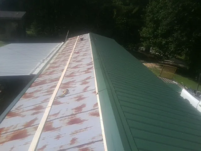 Old rusted panels beside newly installed green metal roofing — Wind Damage Roof Repair by Roofing Brothers in Badin