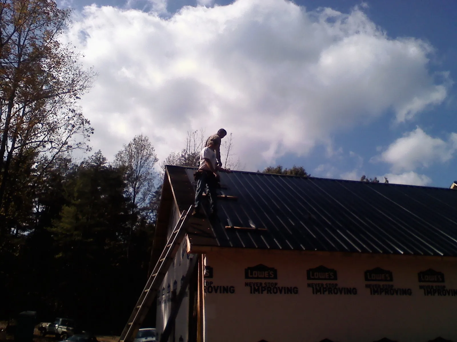 Roofer fastening dark metal panels high against a cloudy sky, from a Roof Inspection job in Badin