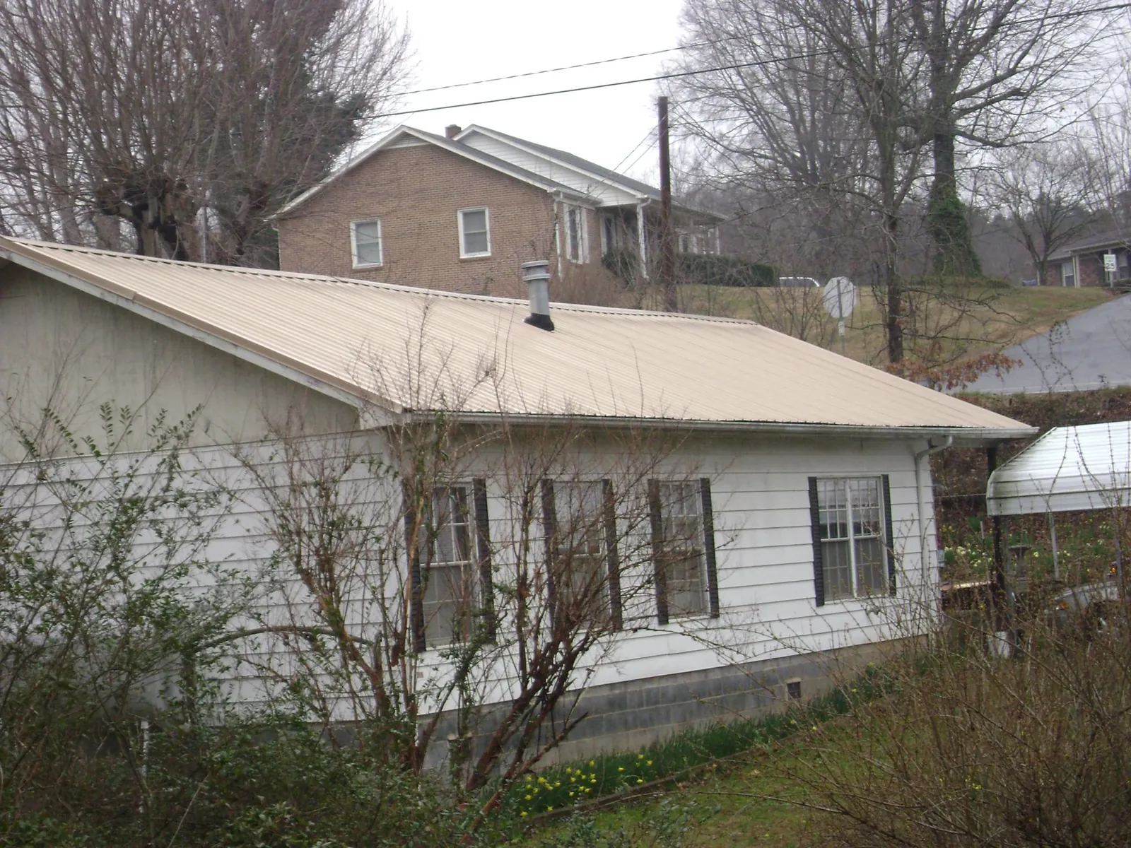 Tan metal roof on a white sided house set into a hillside — Commercial Roofing by Roofing Brothers in Badin
