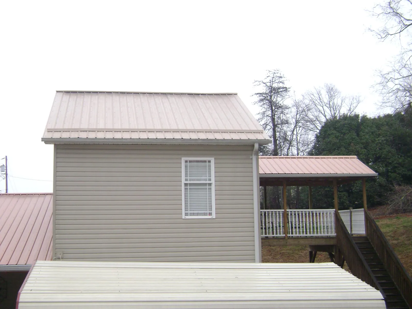 Tan metal roofs on a two story addition and attached porch, from a Roof Replacement job in Badin